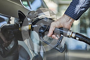 Closeup of a hand filling a fuel tank of a car with fuel dispenser in petrol station