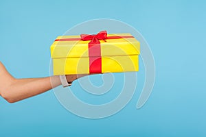 Closeup of hand holding big yellow gift box, congratulations and greeting concept, giving bonus, surprise on birthday photo