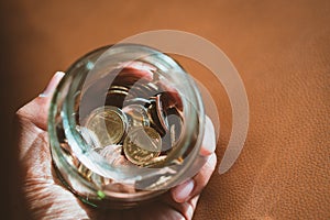 Closeup hand holding coins in glass jar using as financial and m