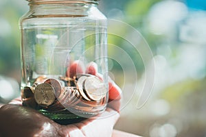 Closeup hand holding coins in glass jar using as financial and m