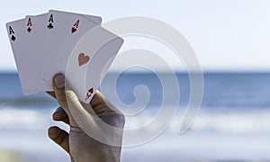 Closeup of a hand holding four ace cards at a beach under the sunlight with a blurry background