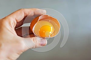 Closeup of a hand holding the shell of a broken egg yolk with a