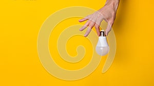 Closeup hand holding white led lighting bulb against a yellow wide background banner with copyspace. concept of idea, energy and