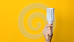 Closeup hand holding white led lighting bulb against a yellow wide background banner with copyspace. concept of idea, energy and