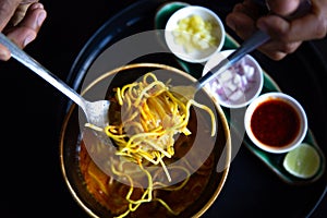 Closeup Hand Holding yellow noodles  spoon,Asian food  noodles  soup  in  bowl on the wooden table vegetable and ingredient