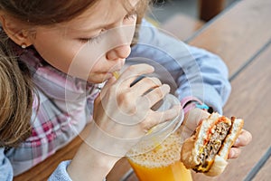 Closeup of hand of kid eating burger and drinking orange juice