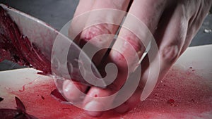 Closeup of hand with knife cutting fresh vegetable. Young chef cutting beet on a white cutting board closeup. Cooking in