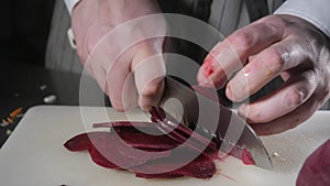 Closeup of hand with knife cutting fresh vegetable. Young chef cutting beet on a white cutting board closeup. Cooking in