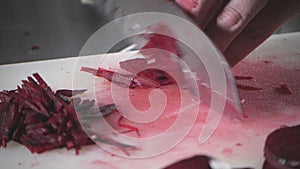 Closeup of hand with knife cutting fresh vegetable. Young chef cutting beet on a white cutting board closeup. Cooking in