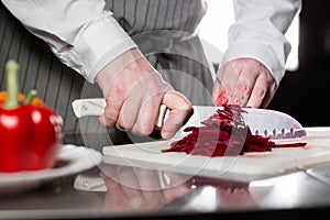 Closeup of hand with knife cutting fresh vegetable. Young chef cutting beet on a white cutting board closeup. Cooking in