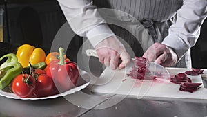 Closeup of hand with knife cutting fresh vegetable. Young chef cutting beet on a white cutting board closeup. Cooking in