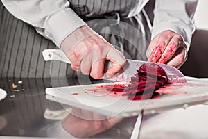 Closeup of hand with knife cutting fresh vegetable. Young chef cutting beet on a white cutting board closeup. Cooking in