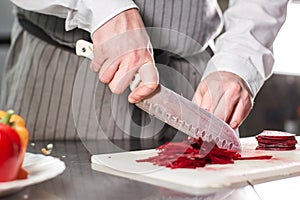 Closeup of hand with knife cutting fresh vegetable. Young chef cutting beet on a white cutting board closeup. Cooking in