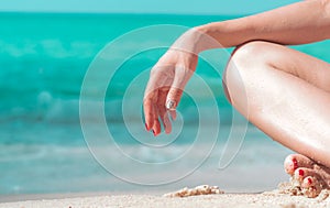 Closeup hand and leg of woman sit on sand beach at seaside with emerald green water. Happy young Asian woman relax and enjoy