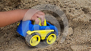 Closeup hand of little child boy playing car toy on sand outdoor in rural nature background.