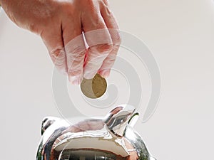 Closeup of the hand of a man placing a coin in a silver piggy bank