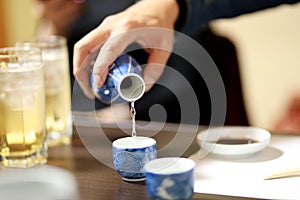 Closeup Hand of man pouring Japanese Sake into sipping ceramic bowl on the wooden table background. Japanese drink style. Warm