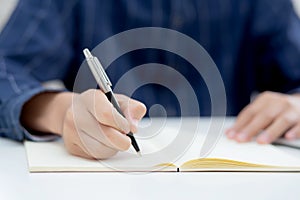 Closeup hand of man writing on notebook with pen on desk, freelance is author, businessman write on notepad on table.