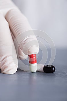 Closeup hand in medical latex glove holding two different capsules on gray table