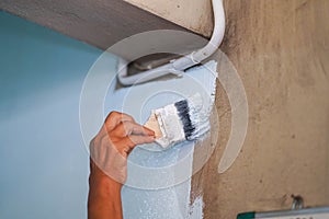 Closeup hand of the painter holding a paint brush painting white colors on the wall in renovation of old house