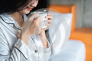 Closeup hand of pretty young woman sitting on the bed and enjoying first morning coffee on sunshine