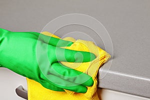 Closeup of a hand in a protective glove holding a napkin and wiping a countertop. Cleaning the kitchen