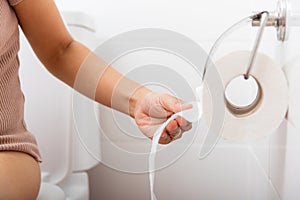 Closeup hand pulling toilet paper roll in holder for wipe.Closeup hand pulling toilet paper roll in holder for wipe, woman sitting