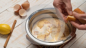 Closeup of a hand putting bread on a bowl of milk, cracked eggshells, lemon, and cinnamon