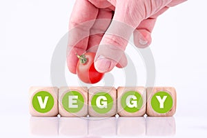 Closeup of a hand putting a cherry tomato on the word Veggy made of wooden cubes
