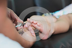 Closeup hand`s mom holding nail clippers, cutting toenails  to daughter girl. Child lying down on  sofa. Baby aged 4-5 years old