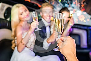 Closeup of hand toasting champagne flute with friends in limousine during party