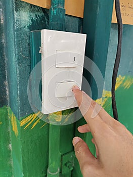 Closeup of hand turning on a light switch on a green wall