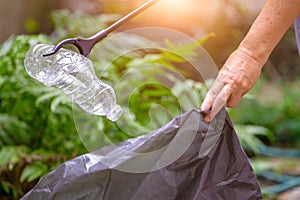 Closeup of hand and waste grabber picking up drinking plastic bottle waste into bag. Ecology and Environmental concerns. Recycling