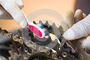 Closeup hand wearing white glove holding toothbrush rubbing on metal bicycle chain, mechanical repair concept