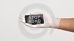 Closeup of the hand in a white sterile glove holding a card with text - STOP ADHD
