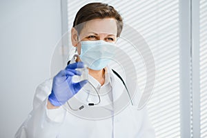 Closeup hand of woman doctor or scientist in doctor& x27;s uniform wearing face mask protective in lab holding medicine