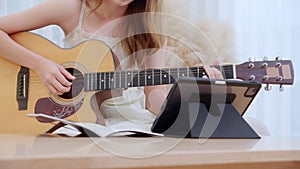 Closeup hand woman sitting on sofa looking tablet and compose a song for practice music with guitar in living room.