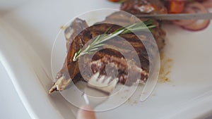 Closeup of the hand of a woman who, with the help of a knife and fork, eats roasted steak in a restaurant.