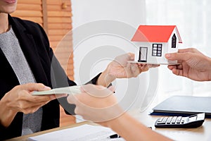Closeup hand of young realtor woman giving house model to hands customer while client giving money with approval.