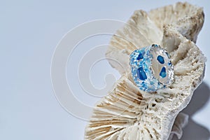 Closeup of handmade ring made of silver metal with blue enamel on top arranged on seashell isolated over light