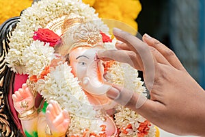 Closeup of hands applying Tilak or Kumkum to Lord Ganesha during Indian religious ganesha or vinayaka Chaturthi festival ceremony