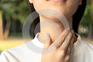 Closeup of hands of asian female people holding her inflamed throat or tonsillitis,child girl touch the neck with her hands,woman photo