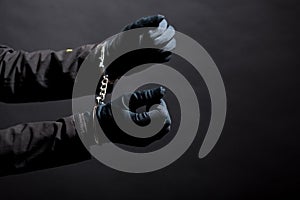 closeup of the hands of a burglar in black gloves with handcuffs on a black background