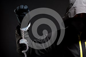 closeup of the hands of a burglar in black gloves with handcuffs on a black background