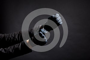 closeup of the hands of a burglar in black gloves with handcuffs on a black background