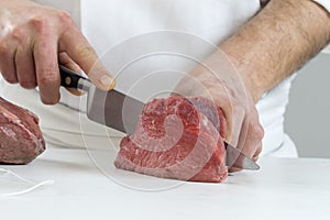 Closeup of the hands of a butcher cutting slices of raw meat off a large loin for tournedos