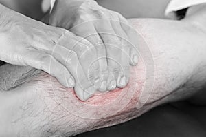 Closeup of hands of chiropractor/physiotherapist doing calf muscle massage to man patient, in silhouette studio. Red color pain.