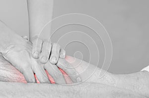 Closeup of hands of chiropractor/physiotherapist doing calf muscle massage to man patient, in silhouette studio. Red color pain.