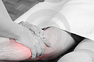 Closeup of hands of chiropractor/physiotherapist doing calf muscle massage to man patient, in silhouette studio. Red color pain.