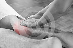 Closeup of hands of chiropractor/physiotherapist doing calf muscle massage to man patient, in silhouette studio. Red color pain.